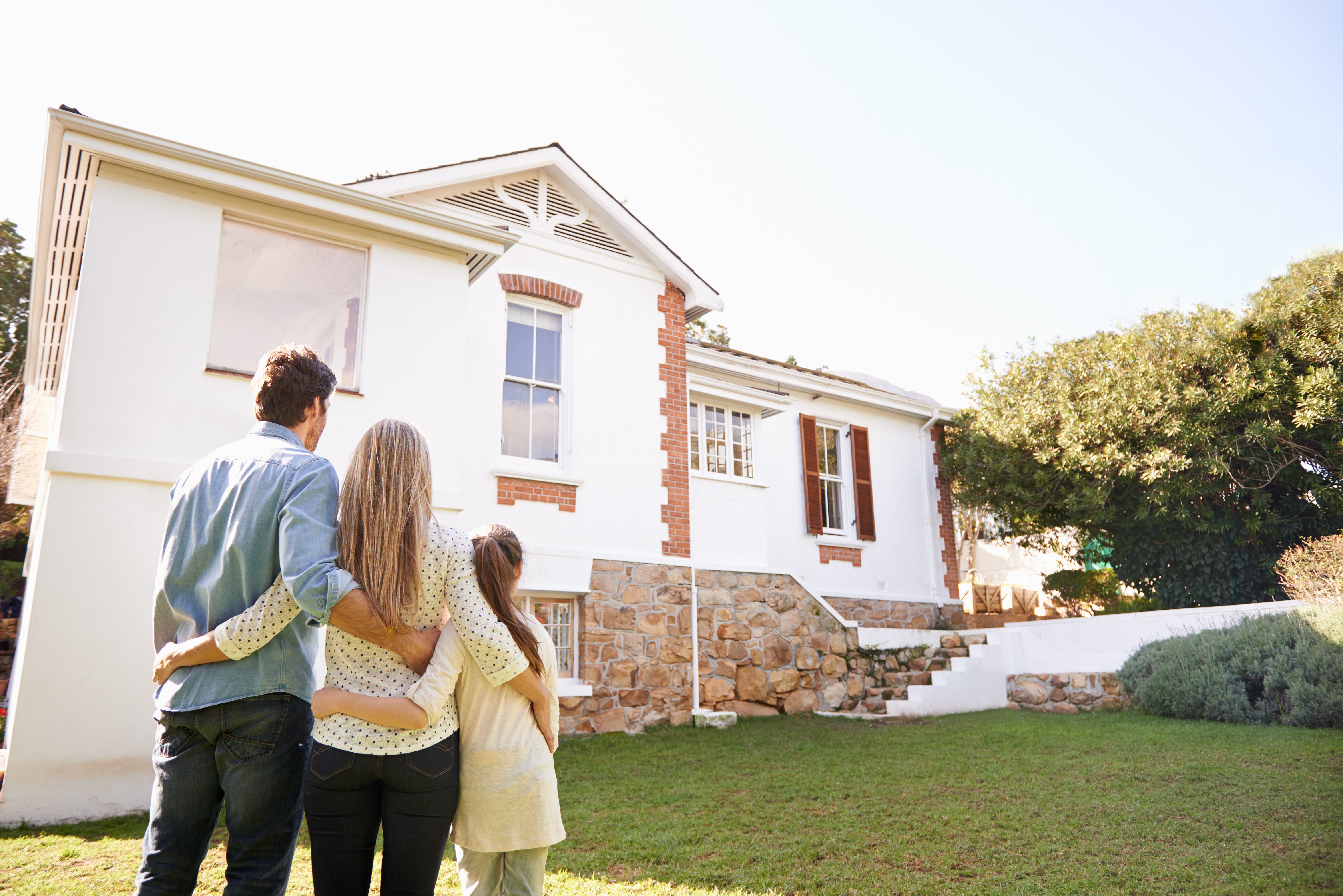 Australian family on a lawn looking at a white and brick house. 