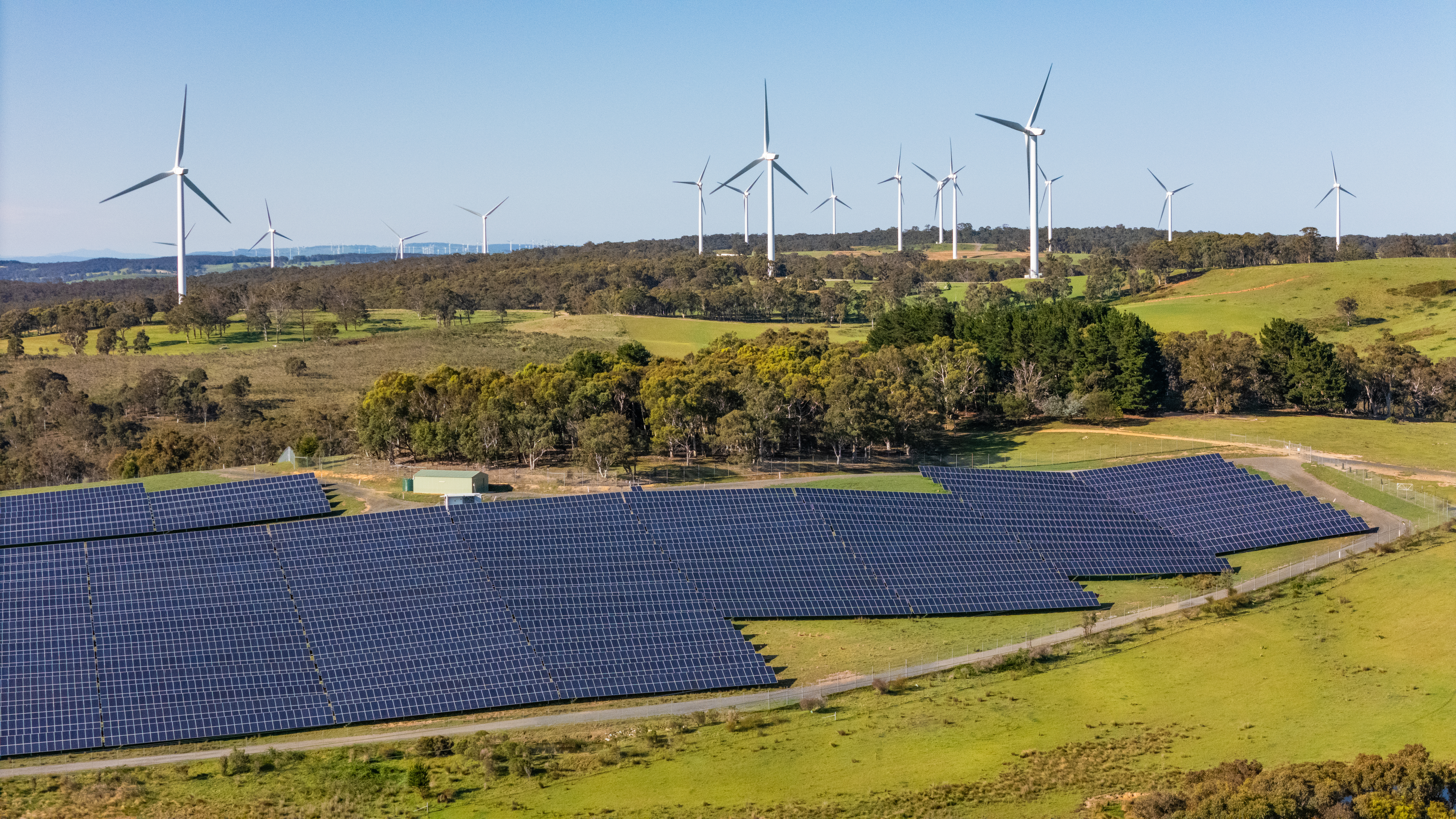 Solar panels in rolling hills with wind farm in background