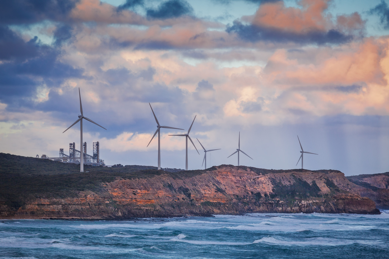 Wind turbines standing on rugged cliff above ocean in Australia at sunset