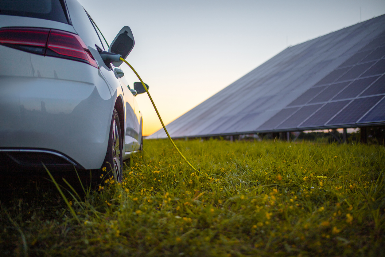 Rear view of white electric car being charged with solar panels in the background