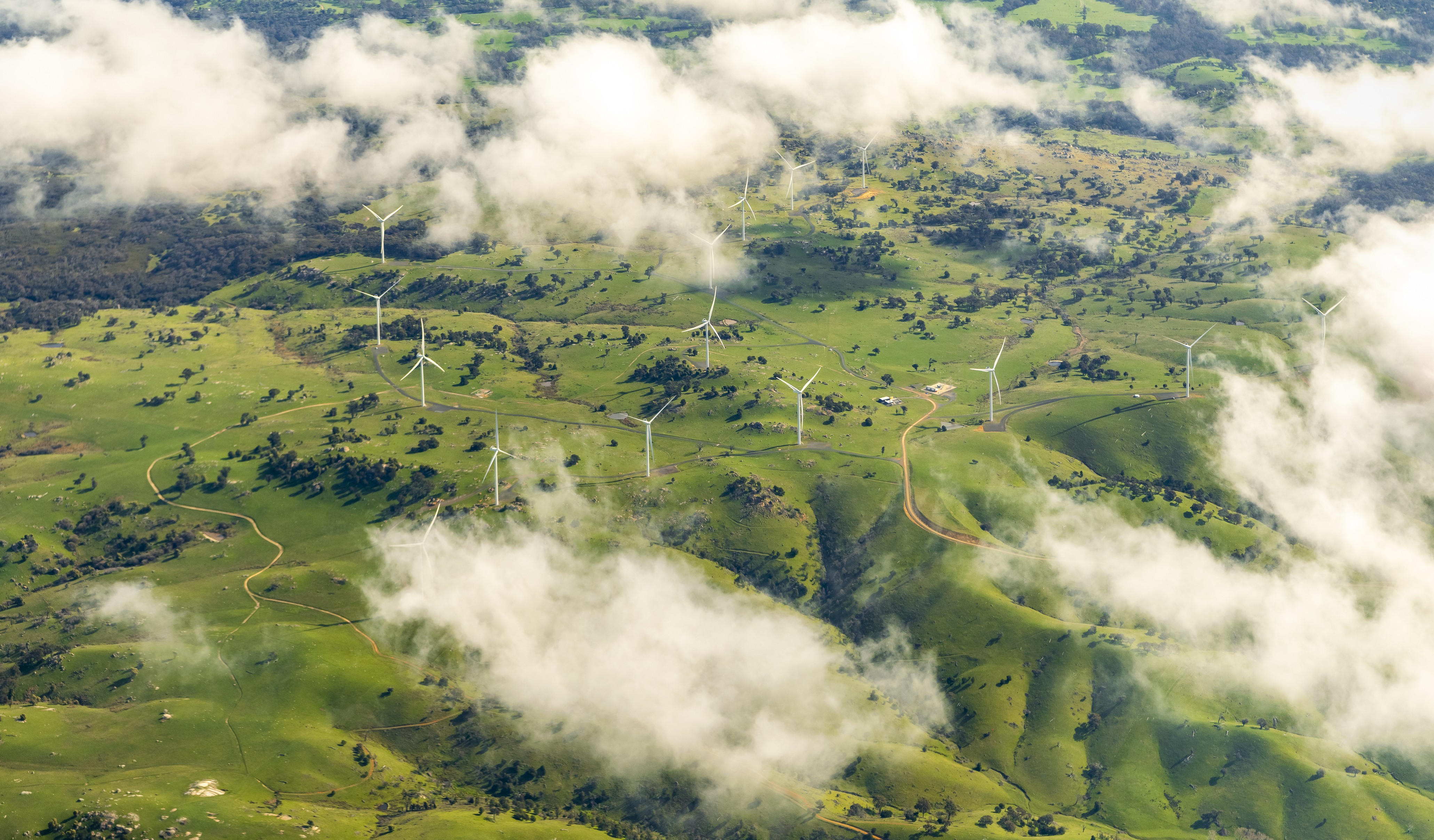 Aerial photograph; A group of wind turbines in an agricultural field from above the clouds