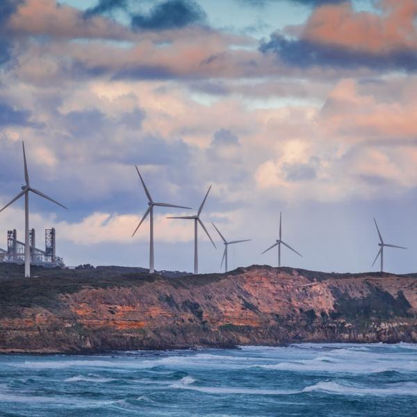 Wind turbines standing on rugged cliff above ocean in Australia at sunset