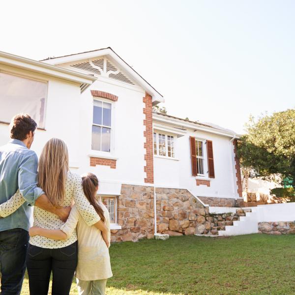 Australian family on a lawn looking at a white and brick house.