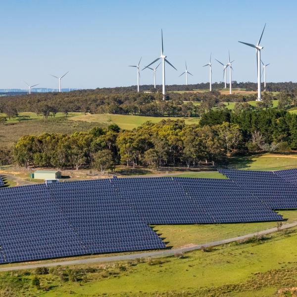Solar panels in rolling hills with wind farm in background