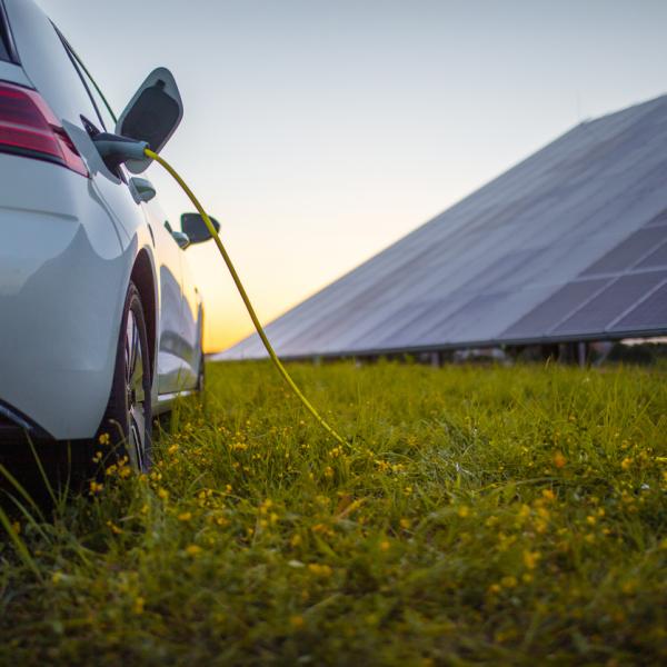 Rear view of white electric car being charged with solar panels in the background