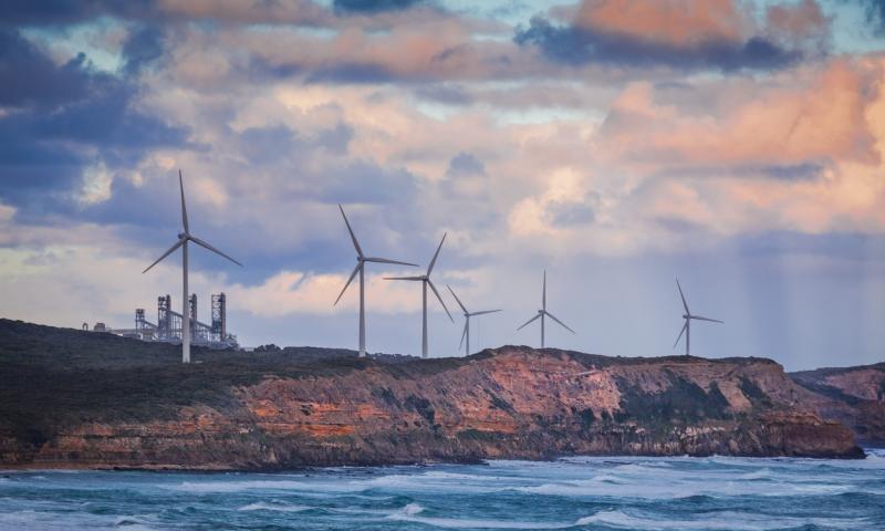 Wind turbines standing on rugged cliff above ocean in Australia at sunset