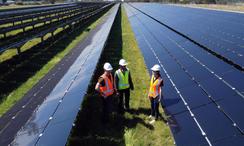 Three Engineers Surrounded By Solar Panels On Solar Farm in Australia. Shot from Drone.