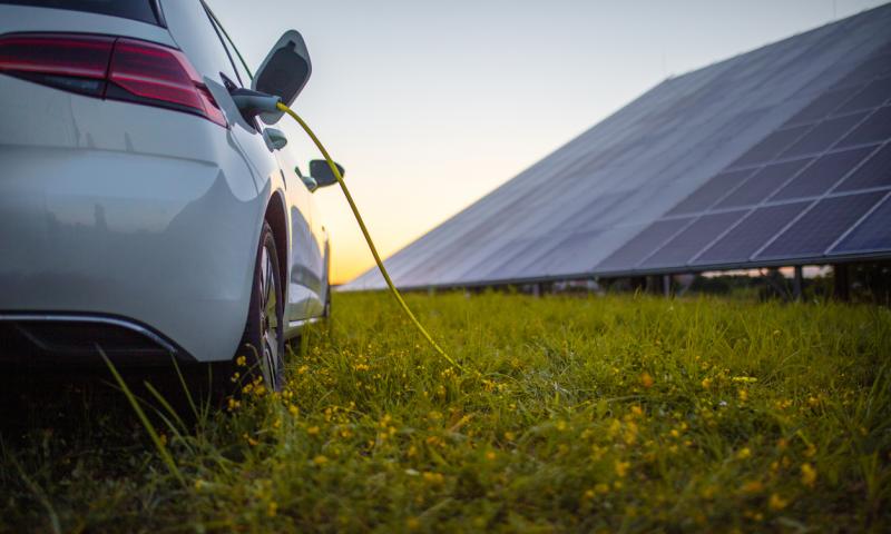 Rear view of white electric car being charged with solar panels in the background
