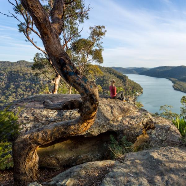 Female sitting on a large rock relaxing in afternoon dappled light the Australian bushland with views over the river