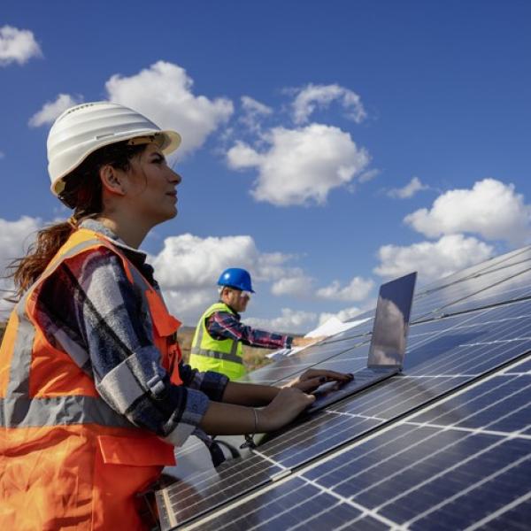 Female tradesperson leaning on a solar panel with blue sky in the background.